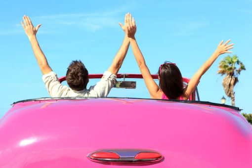 couple in covertible car with hands in the air