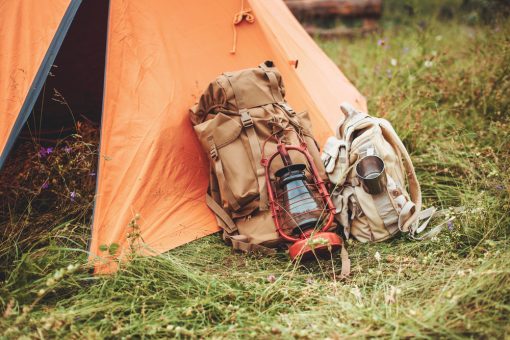 an orange tent and two backpacks near on green grass